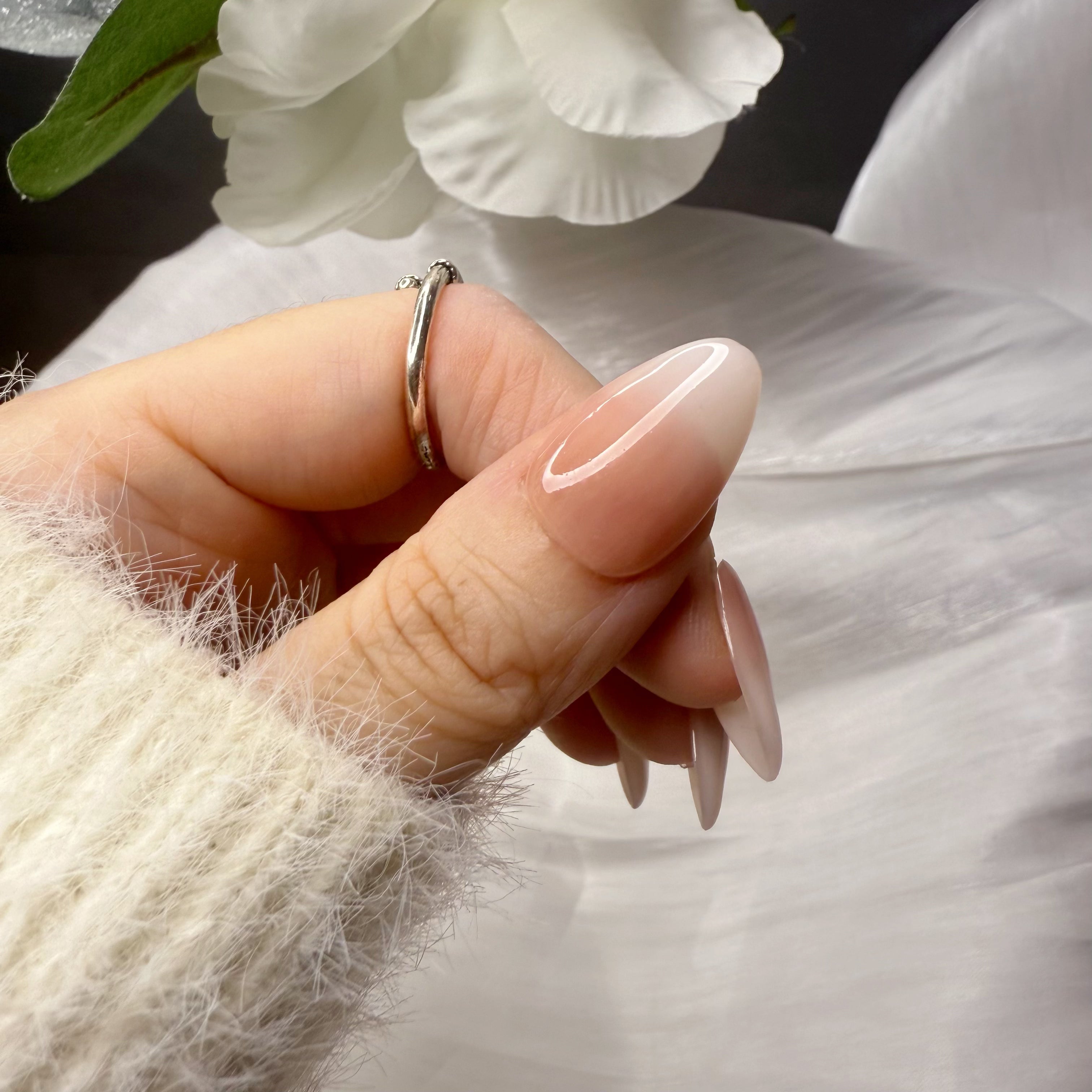 Close-up of a thumb wearing a short almond press-on nail featuring a seamless nude-to-white gradient finish.