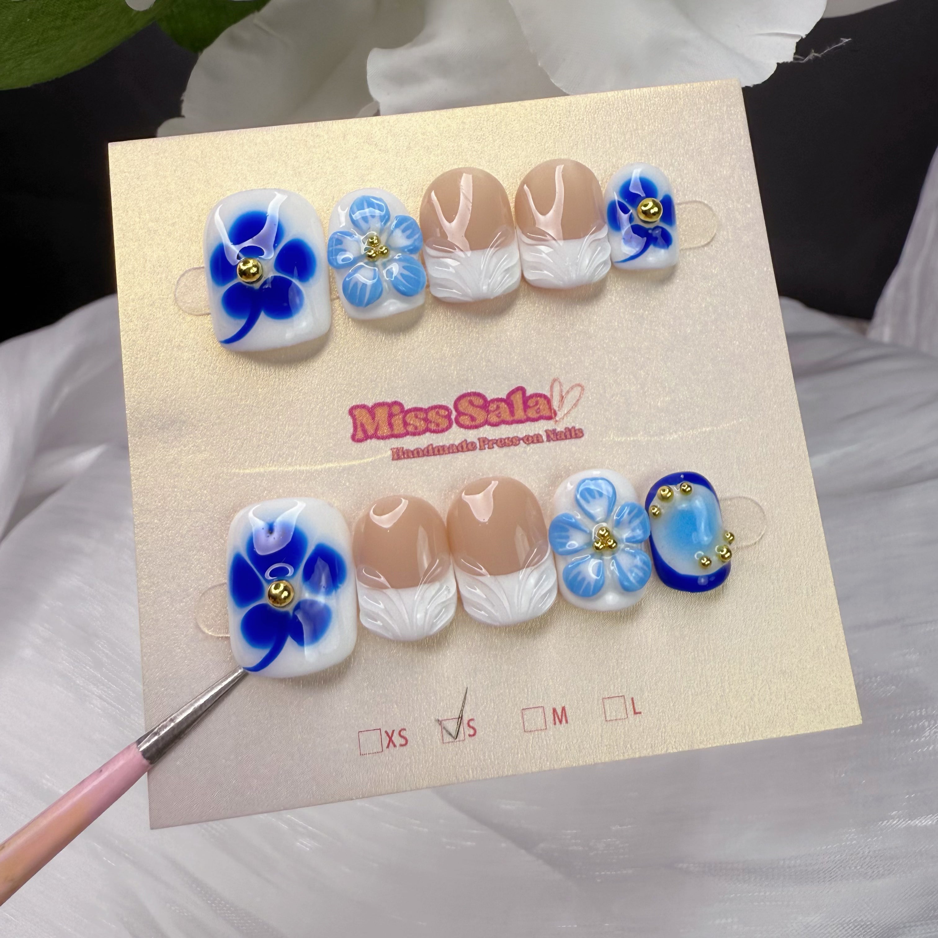 Short Square Press-On Nails with 3D Textured White French Tips, Cobalt Blue Floral Art, 3D Light Blue Flowers, and Gold Stud Accents on a Nude Base