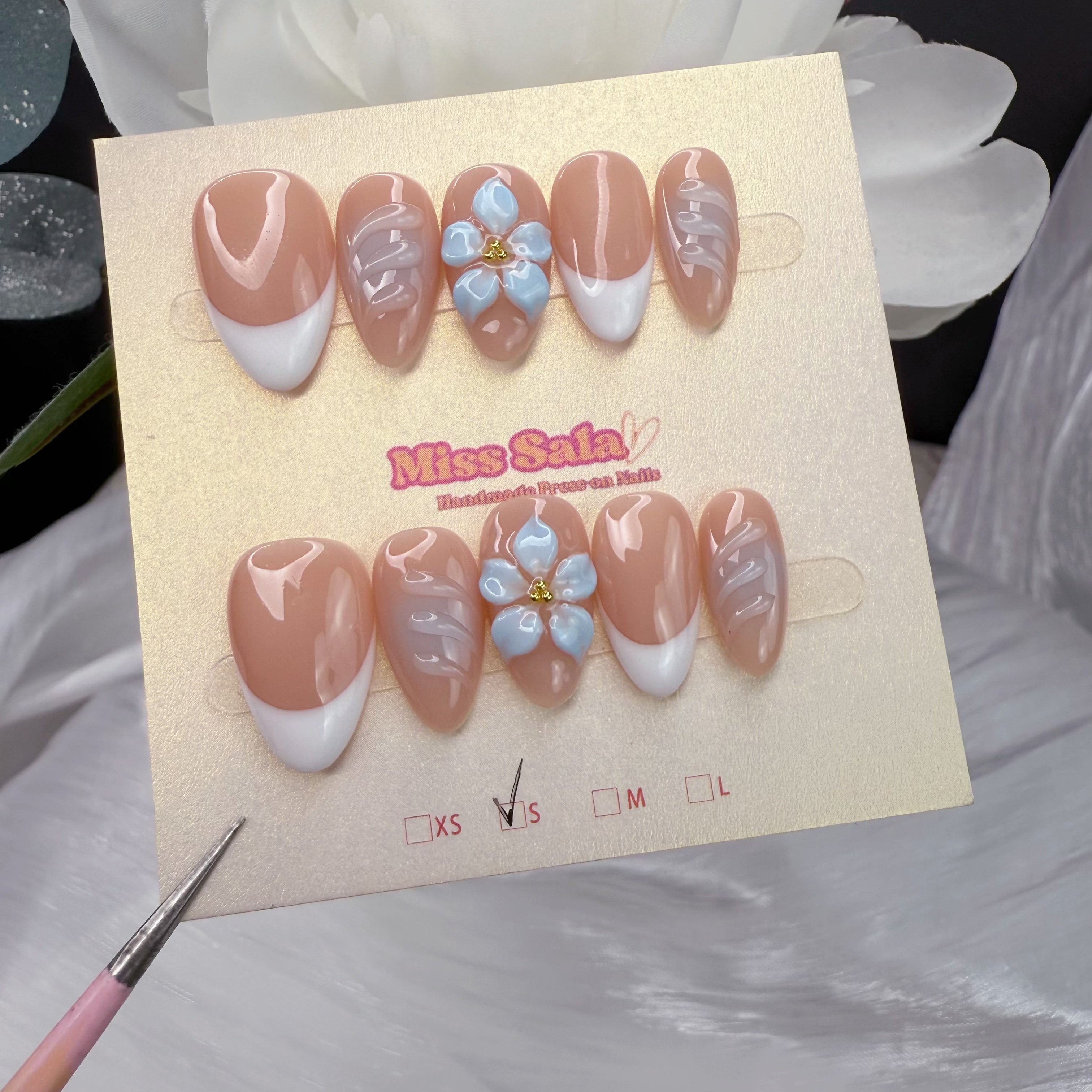 Nude Almond Press-On Nails with White French Tips, a 3D Light Blue Flower with Gold Center, and Raised 3D Ripple Textures