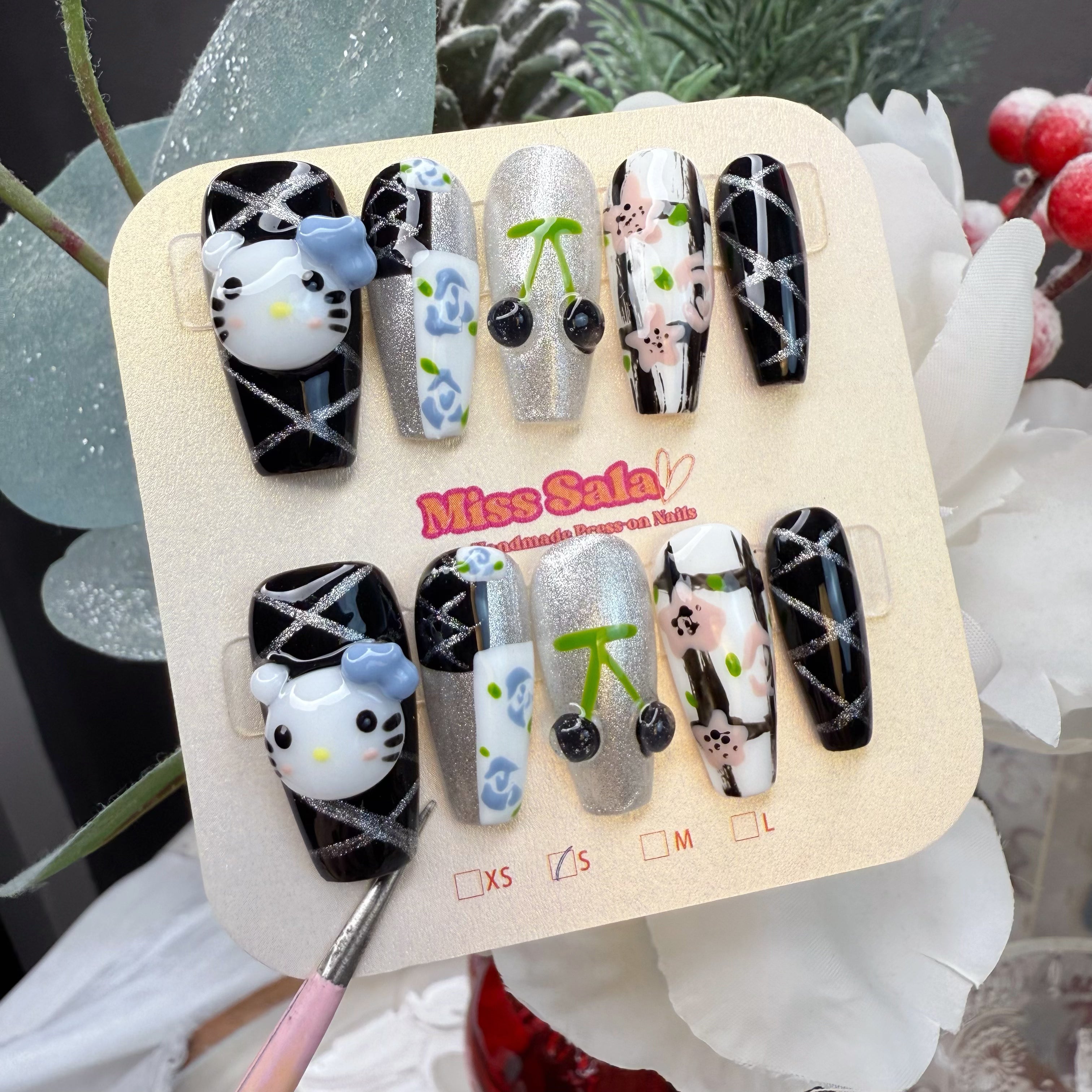 Coffin-Shaped Press-On Nails featuring 3D Kitty Charms, 3D Black Cherries, Silver Glitter Crisscross Patterns, and Hand-Painted Blue and Pink Floral Art