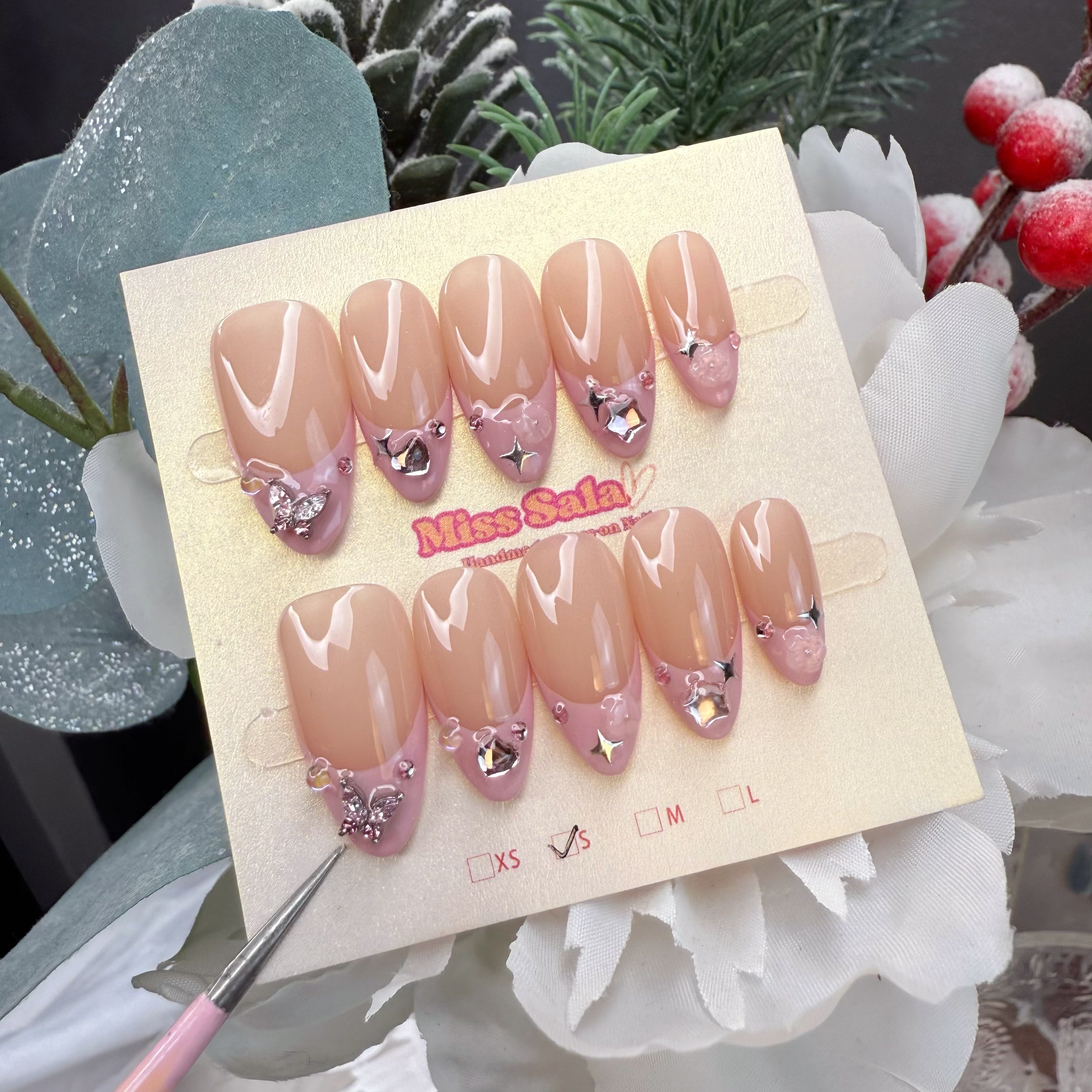 Almond-shaped press-on nails featuring a glossy nude base with soft pink French tips, adorned with 3D silver butterfly charms and sparkling crystal accents.