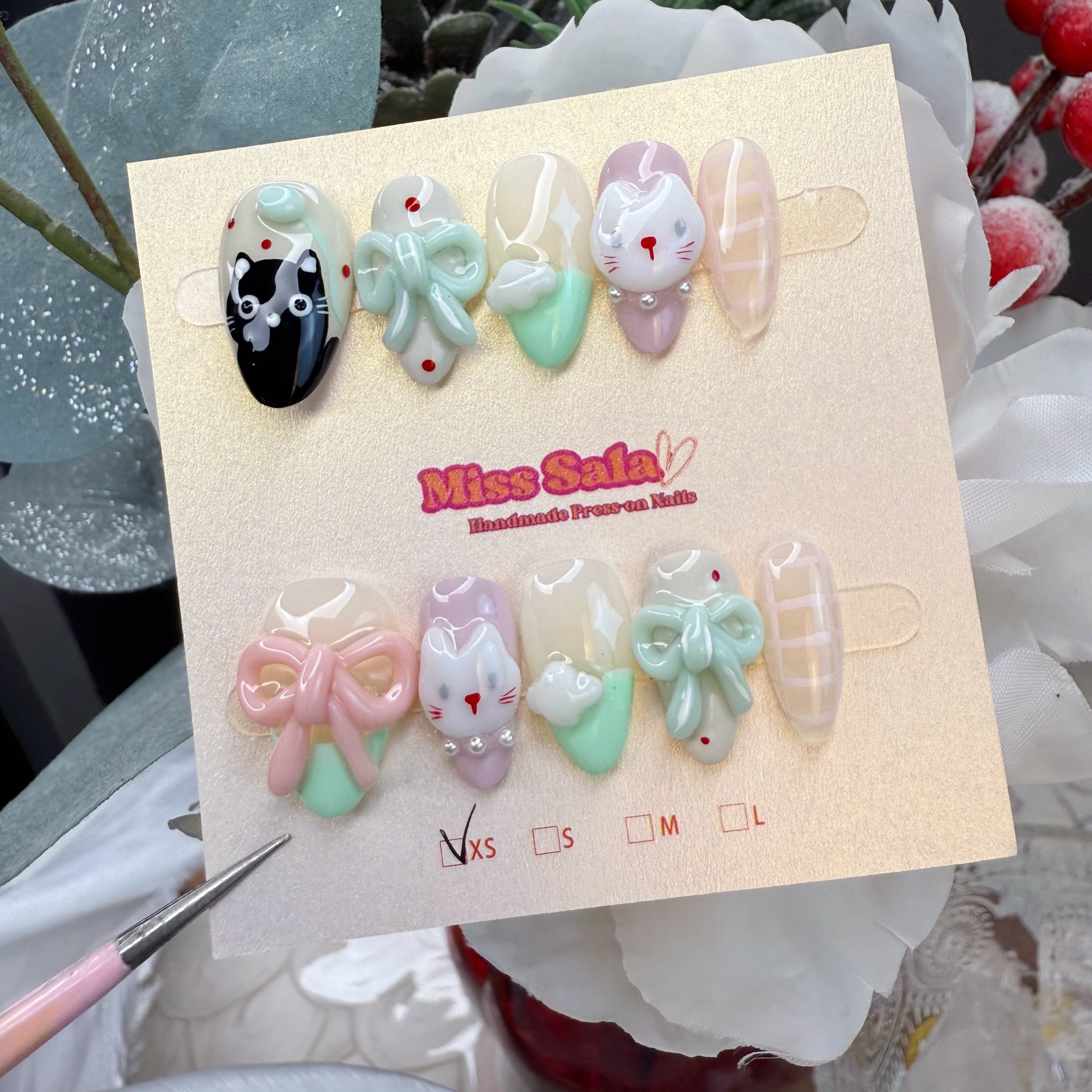Almond-shaped press-on nails featuring various hand-painted cat faces, 3D mint and pink bows, and soft pastel green and lavender accents.