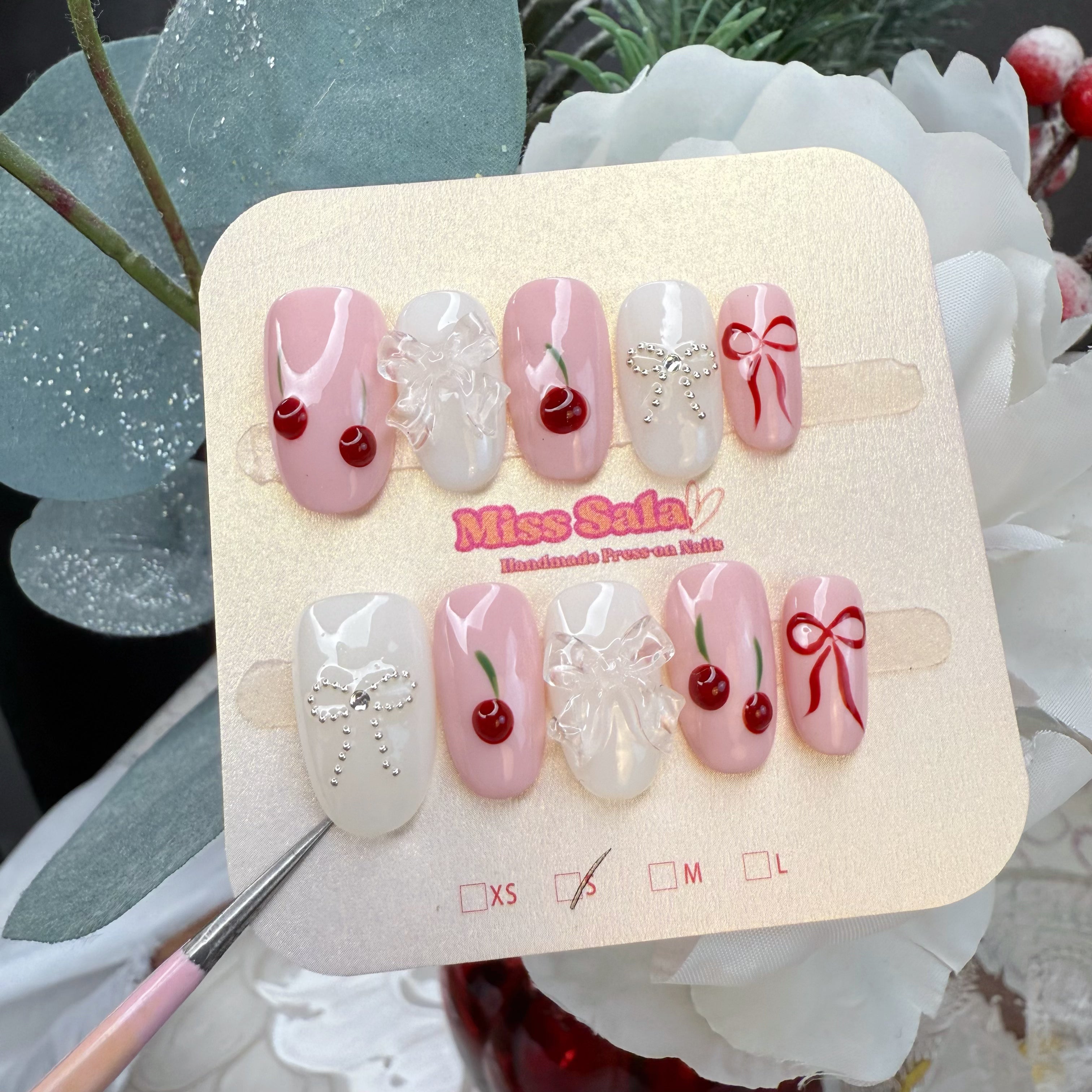 Short Oval Press-On Nails with Baby Pink and White Base, Hand-Painted Red Cherries, Red Ribbons, and a Clear 3D Bow Accent