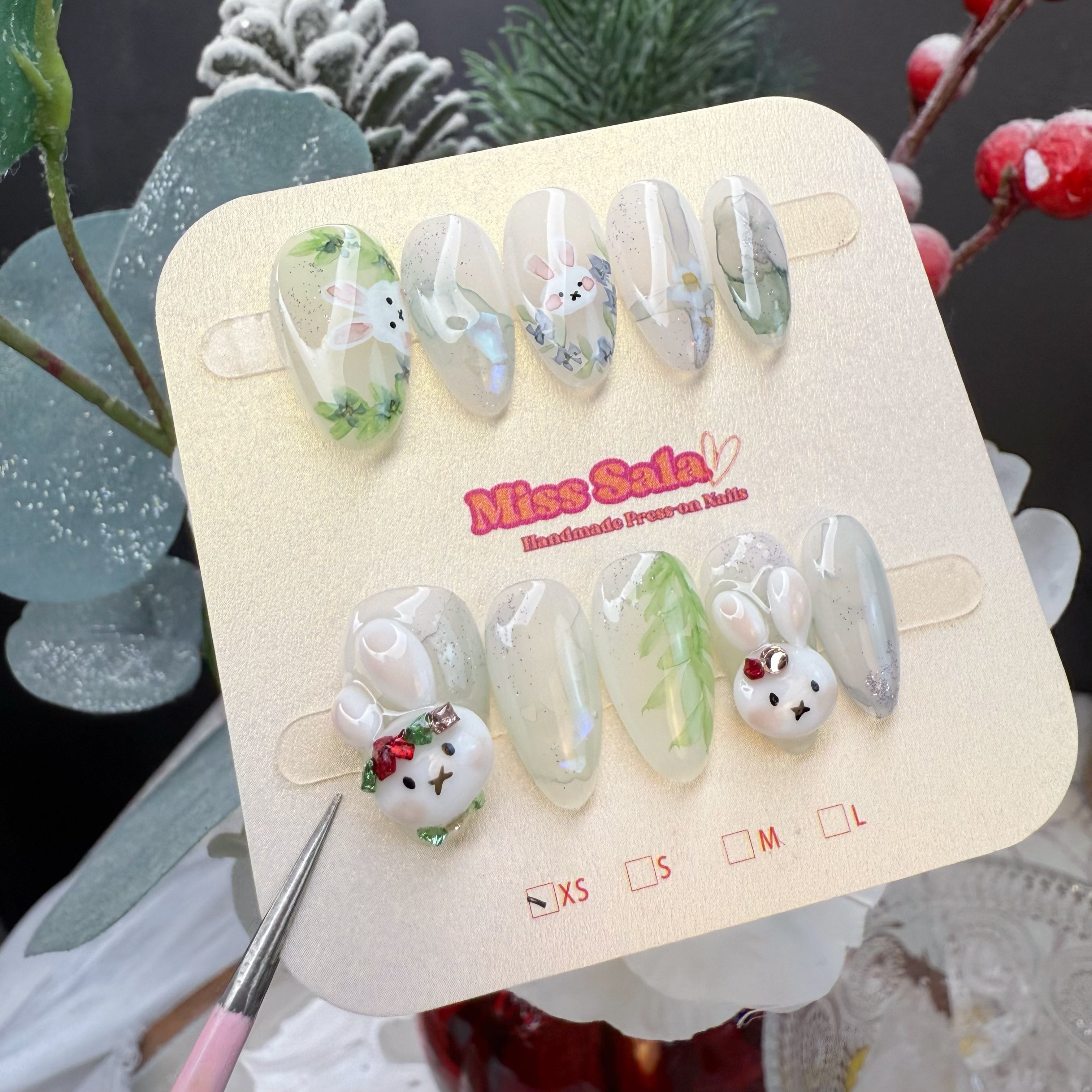 Almond-Shaped Press-On Nails with a Milky Translucent Base, Hand-Painted Green Vines and Tiny Blue Flowers, and 3D White Bunny Charms with Red Bows