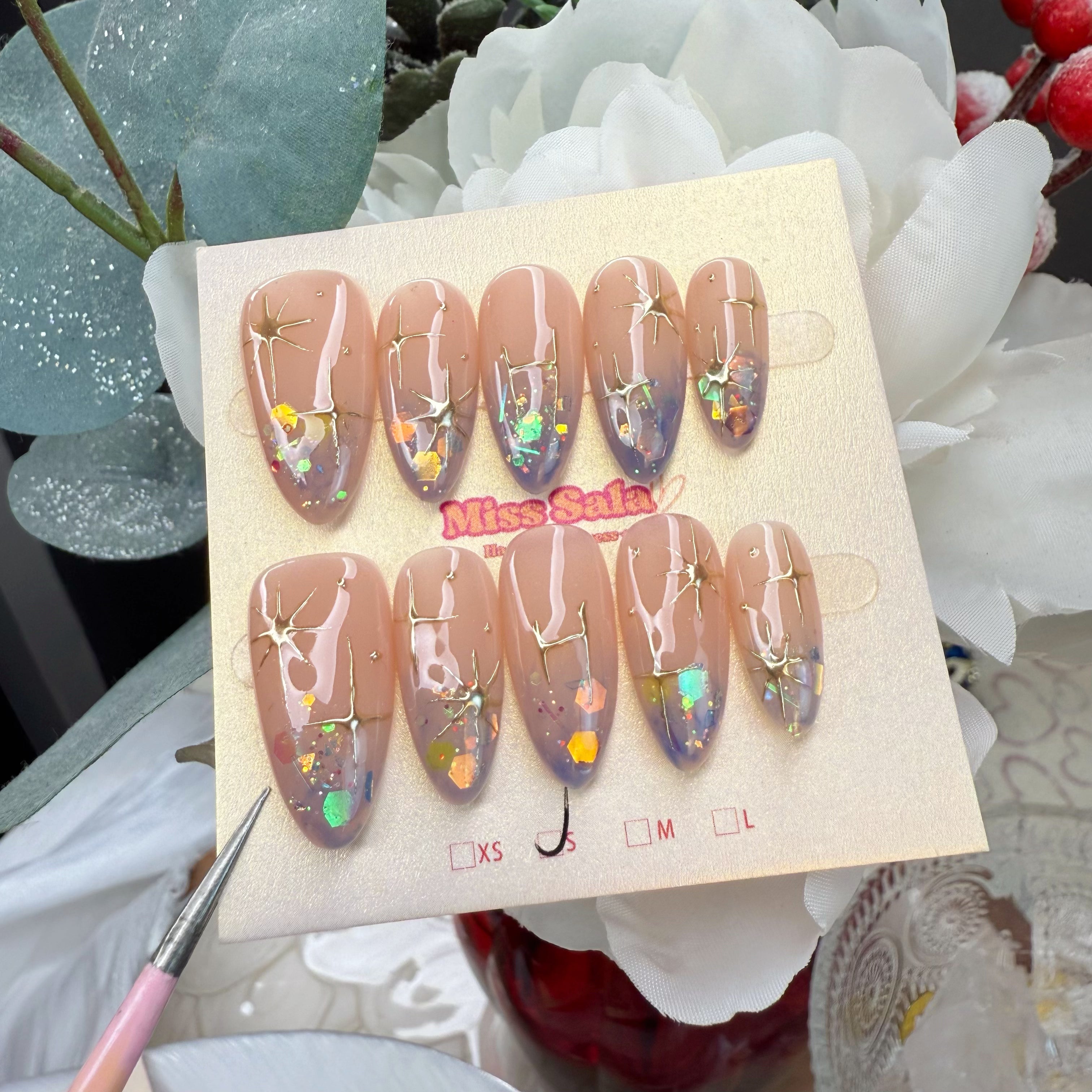 Almond-shaped press-on nails with a nude-to-deep-purple ombre base, featuring hand-painted gold North Star motifs and iridescent hexagonal chunky glitter.