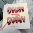 Almond-shaped press-on nails with a glossy nude base and deep red glitter French tips that form a heart shape at the center.