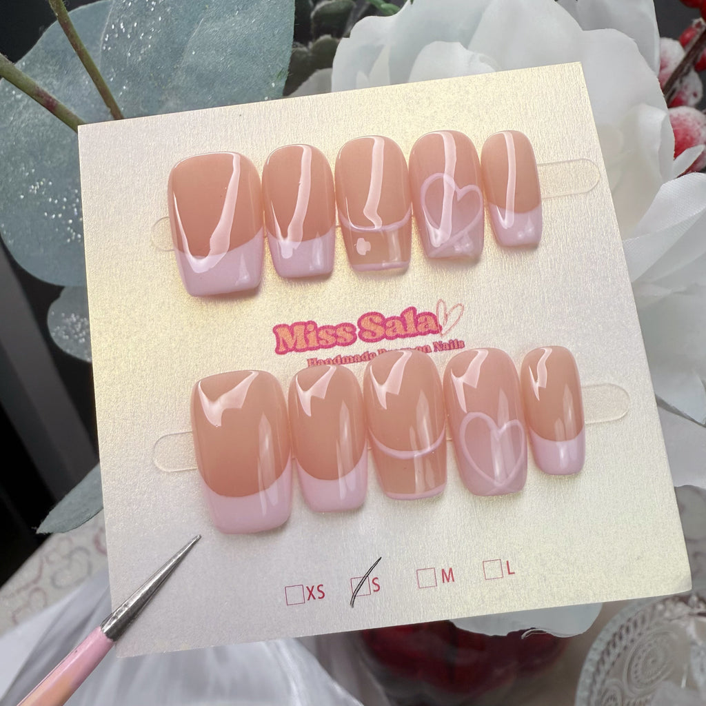 Short square press-on nails featuring a glossy nude base with soft pastel pink French tips and delicate hand-painted white heart outlines.